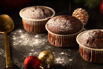 chocolate muffins with powdered sugar on top on a black background. Christmas decoration . Still life close up. Food photo.