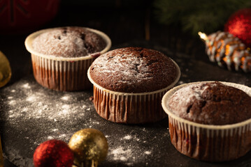chocolate muffins with powdered sugar on top on a black background. Christmas decoration . Still life close up. Food photo.