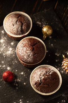 chocolate muffins with powdered sugar on top on a black background. Christmas decoration . Still life close up. Food photo.