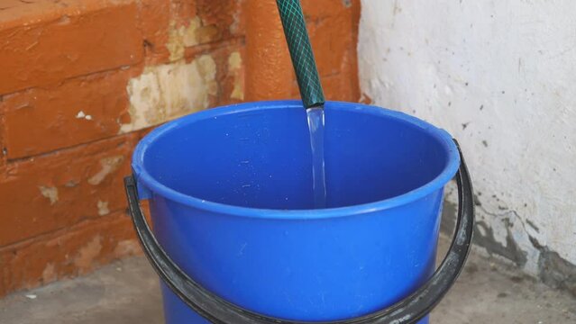 Clear water flows from a hose into a blue bucket. Water is poured into a bucket