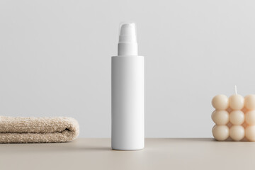 White cosmetic lotion bottle mockup with a candle and a towel on the beige table.