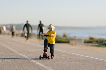 Smiling little boy stands on the road with a scooter