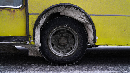 The wheel of a shuttle bus is covered with snow in the winter on the road.
The wheel arches of the bus are filled with snow and ice