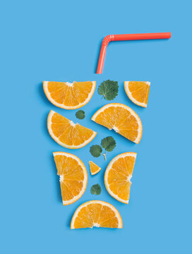 Refreshing summer cocktail concept. Creative flat lay arrangement of orange slices, fresh mint leaves and drinking straw in the shape of a glass with refreshing orange juice on light blue background