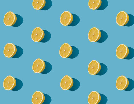Summer pattern made with fresh yellow lemon slice on bright light blue background. Minimal background summer concept on bright sunlight.