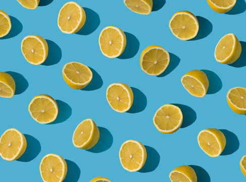 Summer pattern made with fresh yellow lemon slice on bright light blue background. Minimal background summer concept on bright sunlight with sharp shadows