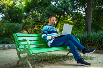 Obraz premium Young indian man working on laptop at park.