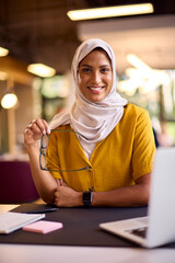 Portrait Of Mature Businesswoman Wearing Headscarf Working On Laptop At Desk In Office