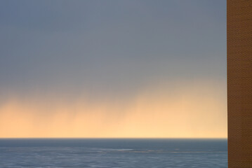  Rain over the sea at sunset, with a brick wall on the left