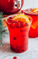 Christmas cranberry punch with oranges in a pitcher and glasses on gray marble table.