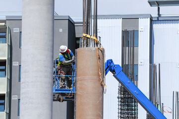 Workers on an aerial lift work on a concrete column at a construction site 