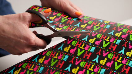 The process of wrapping a gift with women's hands for a birthday in colored gift paper with the inscription 