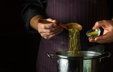 The cook adds dry spices to a pot of boiling food. Retsoran kitchen cooking concept with...
