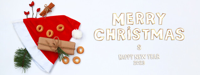 Fototapeta na wymiar Merry Christmas and Happy New Year 2023, Christmas card or banner. Red cap, gift, spruce branch, bagels and cinnamon tubes on a white background
