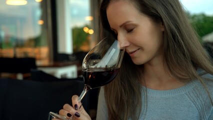 Woman drinking red wine from wine glass in restaurant or cafe. Expert tasting, smelling wine.
