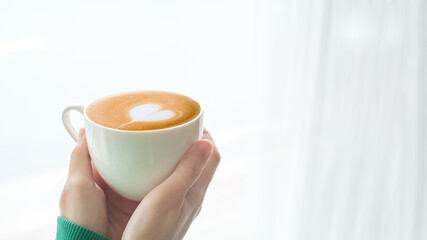 Beautiful girl in green sweater holding cup of tea or coffee in the morning. Closeup of female hands holding a mug of beverage.