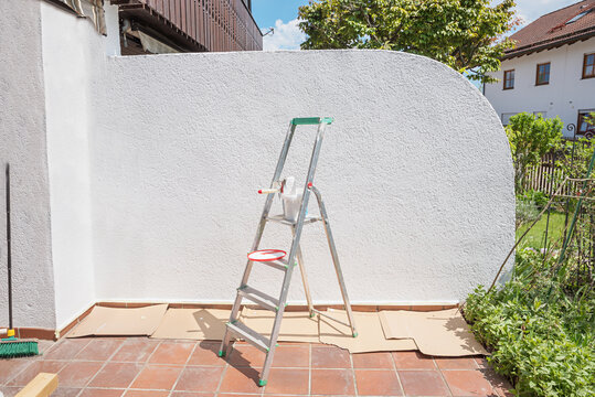 fresh white painted separating wall at the patio. Ladder with painting tools.