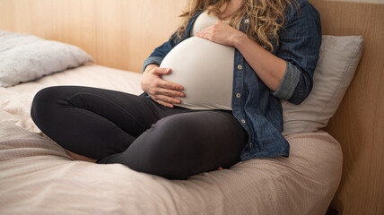 Pregnant woman sitting on bed holding her belly