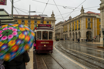 Oczekiwanie na czerwony tramwaj, typowy transport publiczny w Lizbonie. Plac Comercio w Lizbonie, Portugalia w deszczowy, pochmurny dzień. - obrazy, fototapety, plakaty