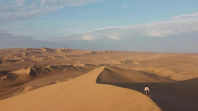 Man walk on edge of dunes. Slow dunes reveal. Aerial view of Huacachina Oasis, in the desert sand dunes near the city of Ica, Peru