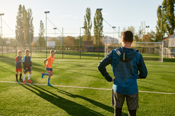 Kids practicing soccer on grass field under football coach control