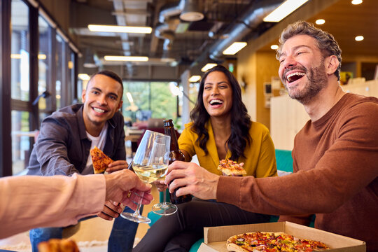 Staff At Informal Meeting In Office With Takeaway Pizza And Drinks