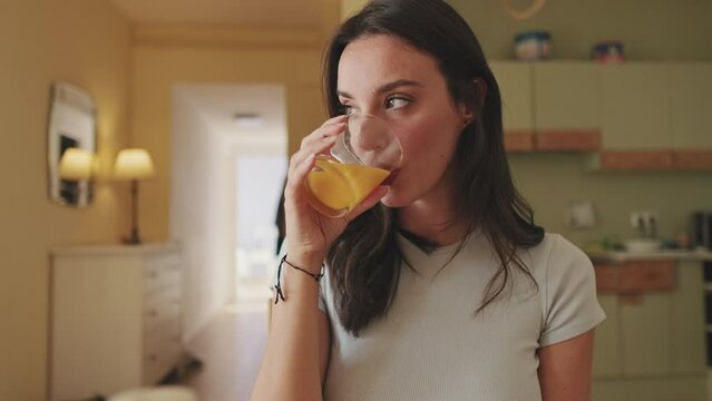 Close up, young woman drinking orange juice while sitting in the kitchen