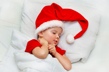 Little boy sleeping on white linen in the Santa hat.	