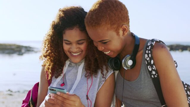 Friends, funny meme on social media and smartphone, travel and connection on beach adventure, internet comic and technology. Young women, comedy and communication online, traveling and laugh outdoor.