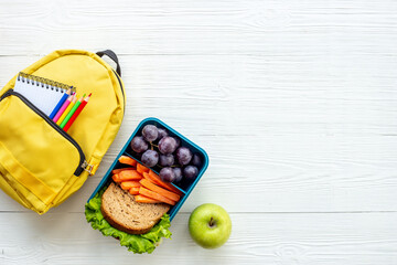 School lunchbox with fruits and yellow backpack, top view