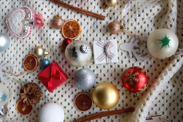 Fototapeta na wymiar Various colorful Christmas ornaments, small presents and seasonal spices on white knitted blanket. Top view.