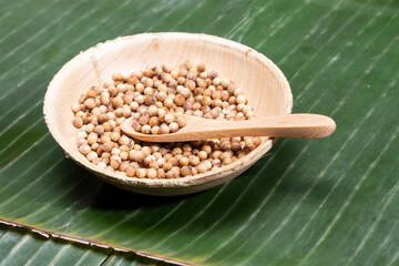 Coriander seeds in a bamboo bowl on banana leaf.