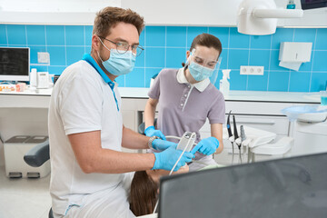 Serious focused stomatologist examining client teeth using modern equipment