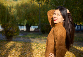 Beautiful young woman in a brown coat in the autumn park holds her hair by hand. Selective focus.