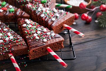Fototapeta na wymiar Chocolate brownies Christmas tree with chocolate icing and festive sprinkles on wooden table. Christmas food ideas sweet homemade Christmas holidays pastry concept. Holiday cooking concept. Top view.