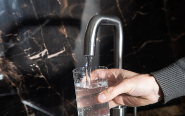 Man filling glass with water from tap in kitchen.