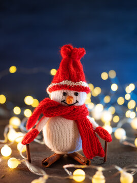 knitted snowman on skis made of cinnamon sticks. christmas bright bokeh garland background