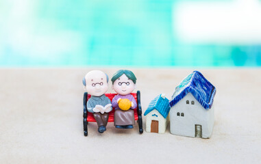 Obraz na płótnie Canvas Miniature elderly couple sitting on the bench with house model, eldery home care concept