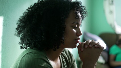 A hopeful Brazilian young woman praying at home. An African South American person having FAITH