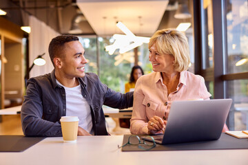 Mature Businesswoman Mentoring Younger Male Colleague Working On Laptop At Desk