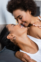 joyful and lesbian african american woman with closed eyes kissing girlfriend on bed.