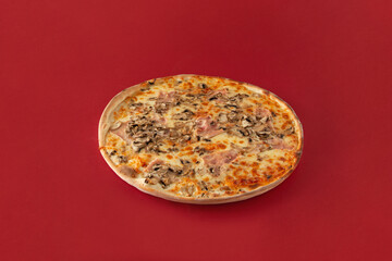 Whole tasty pizza standing on isolated dark red background. Minimal abstract concept of traditional Italian baked food. An idea for a restaurant or pizzeria card. A high-calorie fast food meal.