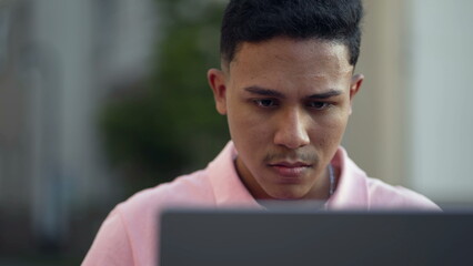 One young hispanic man closeup face looking at computer laptop outside