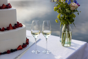 wedding cake with berries and cream on the lakeshore with two glass of white wine and a little 
colorful bunch of flowers