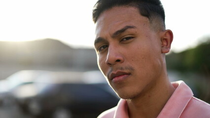 One serious young hispanic man standing outside looking at camera. Portrait of a casual confident South American Brazilian guy closeup face