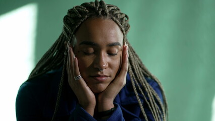 Naklejka premium One pensive young black woman in contemplation. Thoughtful African American pensive adult girl with dreadlocks closeup face
