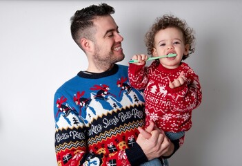 Man holding his beautiful little son with curly hair wearing red Christmas knitted sweater against...