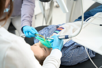 Doctor with assistant in dental office is treating teenager tooth