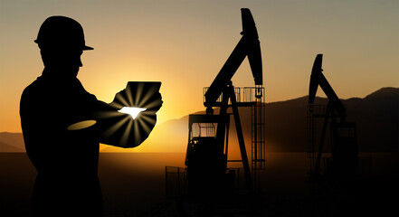 Silhouette of engineer with a digital tablet on the background of oil rigs