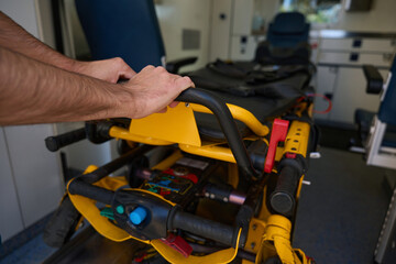 Man holds onto handrail of stretcher in modernly equipped ambulance